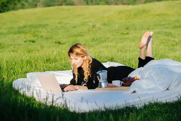 Vrouw genieten van het werken op laptop, liggend in bed buiten, onder zachte lente zon — Stockfoto