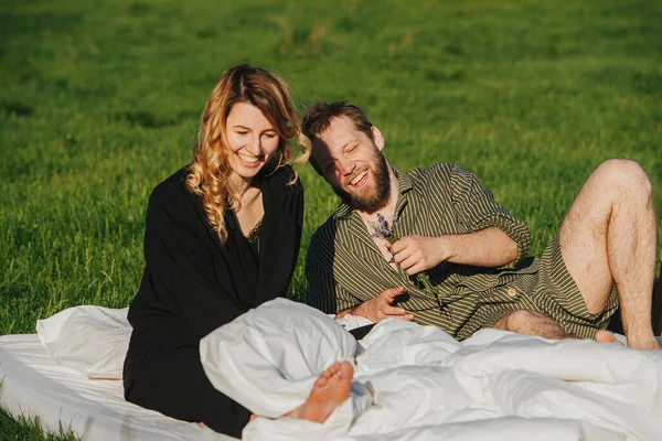 Pareja sonriente en la cama hecha al aire libre sobre una hierba en un campo, después de despertar —  Fotos de Stock