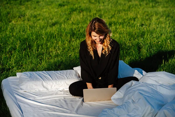 Tevreden, tevreden vrouw werken op laptop, zitten cross-legged in bed buiten — Stockfoto