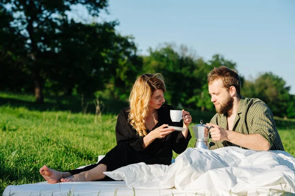 Pareja bebiendo té en la cama al aire libre en una hierba en el campo bajo un cielo azul —  Fotos de Stock