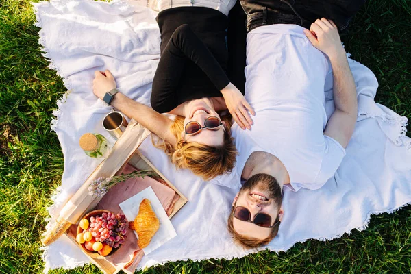 Pareja feliz descansando sobre una manta durante el picnic al lado de la caja de comida —  Fotos de Stock