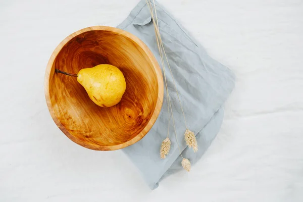 Pera madura en un tazón de madera, de pie sobre una servilleta sobre un blanco. Vista superior . — Foto de Stock