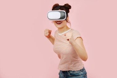 VR kulaklıklı, tuhaf gülümseyen genç bir kadın. Muharebe pozisyonu almış, yanlamasına duruyor, yumruklar havada, biri önde, biri arkada..