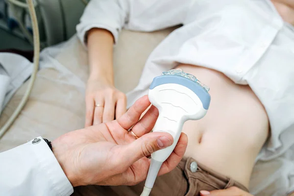 Doctor performing abdominal ultrasound scan on a young female patient. He\'s holding probe lubed with gel, ready to get down to business. Cropped, no heads.
