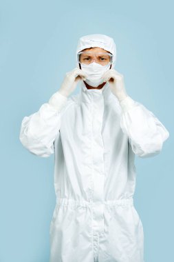 Maske, eldiven ve gözlük takan beyaz kostümlü bir doktor.