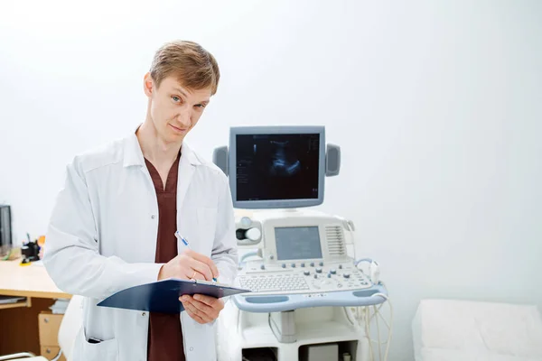 Jeune médecin sceptique écrivant sur vous à côté d'une machine à échographie — Photo