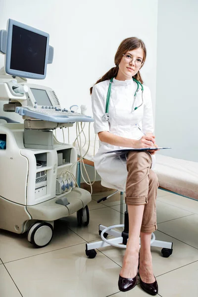 Portrait of young female doctor in glasses doing paperwork in diagnostic cabinet — Stock Photo, Image