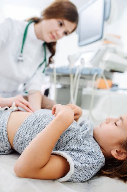 Genç bayan doktor parmaklarını küçük bir kızın karnına bastırıyor. İç organlarını kontrol ediyor. Elleri göğsünde, gözleri kapalı yatan bir kız. Bulanık, kıza odaklan..