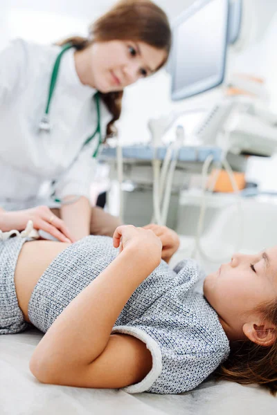 若い女医は少女の胃に指を押し当てている 彼女は内臓を調べてる 胸に手を置いて横になって目を閉じている少女 彼女に焦点を当てて — ストック写真