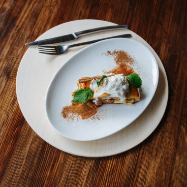 Bir şefin servis ettiği bir parça elmalı pasta. Üst Manzara. Üstüne ekşi krema, nane ve tarçın. Yan tarafında çatal bıçak olan yuvarlak bir tahtada tabak..