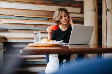 Kafenin köşesinde laptopunu izlerken kahve içen çekici genç bir kadın. Koyu sarı omuzlu, uzun saçlı. Tek başıma oturuyorum..