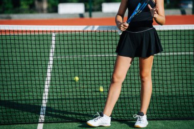 Güneşli bir günde yepyeni bir tenis kortunun ortasında spor kıyafetli genç bir kızın alt kısımları. Üstü kısa tenis eteği giyiyor..