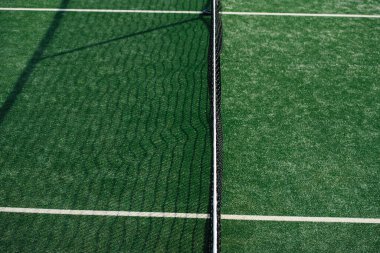 Tenis kortunun ortasında yeşil işaretler ve iki taraftan birinde ağ gölgesi var.