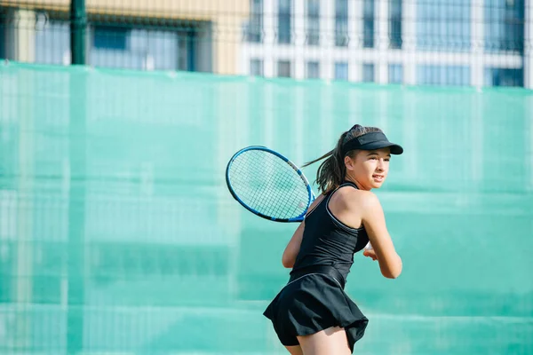 真新しいコートでテニスをする黒のスポーツ服の少女は ボールを返す準備ができています フェンスや高層マンションを覆う旗の上に — ストック写真