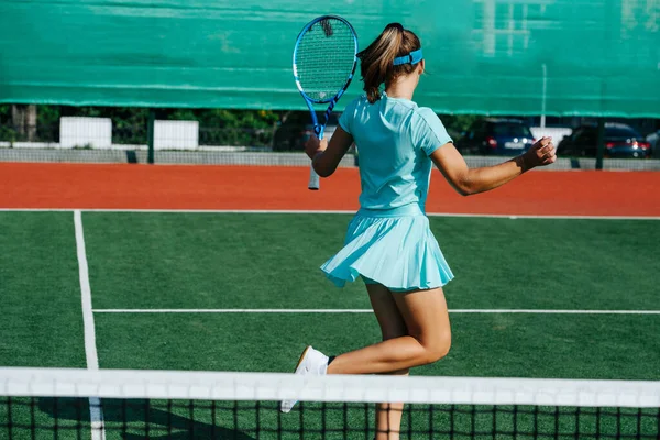 空の青のスポーティな衣装を着た10代の女の子は 楽しさを好み ダンスをし テニスコートでジャンプし 休憩を取ります フェンスを覆う旗の上に — ストック写真