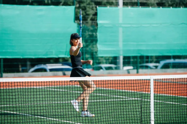 新しいテニスコートで黒のスポーツ衣装のトレーニングで10代の女の子は ラケットで遊んで それを保持します フェンスを覆う旗の上に — ストック写真