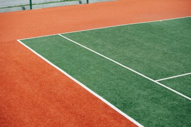 Yeşil iç tenis kortunun köşesinde beyaz lekeler ve kahverengi dış kısım var. Düşük açılı çekim.