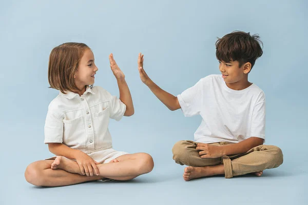 Niño y niña de aproximadamente la misma edad sentados en el suelo con las piernas cruzadas — Foto de Stock