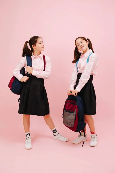 漂亮的双胞胎女学生高兴地摆姿势 看着相机 低角度 粉红背景 工作室拍摄 一个手拿着她的背包 另一个手拿着她的背包 — 图库照片