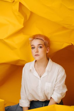 Bacaklarının üzerinde oturan şehvetli genç bir kadın. Etrafına sarılı sarı kağıtların üzerine. Kısa boyalı sarı saçları ve yıldız makyajı var. Kameraya bakıyorum..