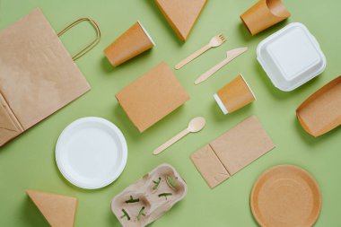 Çevre dostu tek kullanımlık bulaşık takımı ve yeşil arka planda bambu kaplar. Kağıt ve mısır nişastası kutuları, fincanlar, paketler ve tabaklar. Üst görünüm.