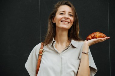 Mutlu olgun bir kadın avucunun içinde taze pişmiş kruvasan tutuyor. Dışarıda, şirket kıyafetleri giyiyor..