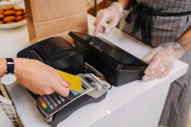 Kadın alışveriş yapıyor, kredi kartıyla ödüyor. Baker kasanın arkasında duruyor ve fiyatı hesaplıyor. Kesildi, kafası yok..