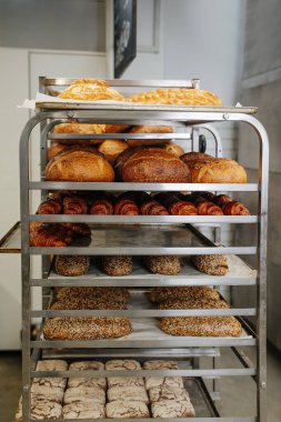Demir bir rafta tepsilerle soğutulmuş taze pişmiş ekmeklerin çeşitliliği