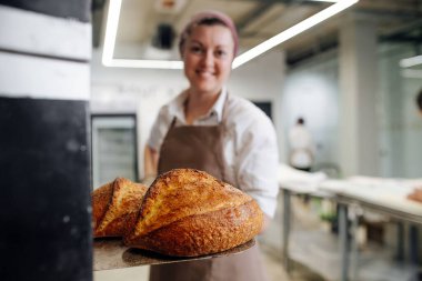 Dişi fırıncı, özel bir kürekle taze ekmek basıyor. Saç bandı takıyor. Ekmeğe odaklan..