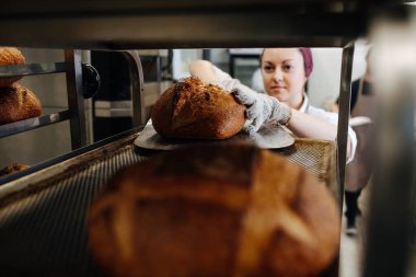 Dişi fırıncı, özel bir galeri kullanarak taze ekmeği rafa koyuyor. Saç bandı takıyor. Görüntü şeften alındı.