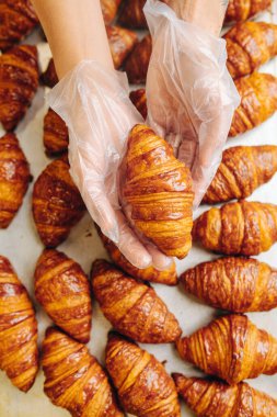 Baker, üzerinde bulundukları yüzeyden taze pişmiş altın kruvasan alıyor. Avuçlarında bir tane tutuyor. Üst manzara, yukarıdan çekim