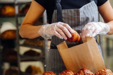 Baker, taze pişmiş altın kruvasanları teslimat için kese kağıdına koyuyor. Ön görünüm