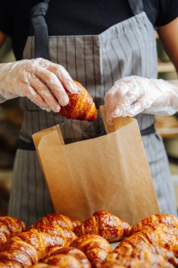 Baker, taze pişmiş altın kruvasanları teslimat için kese kağıdına koyuyor. Ön görünüm