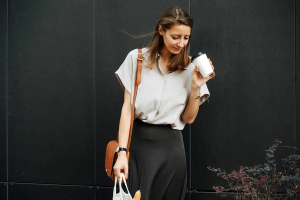 Mature woman in corporate clothing standing on the street. She's looking down inside empty coffee cup