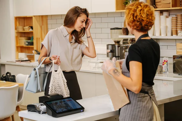 Mevcut mallara bakan genç bir kadın, fırıncı kadın yazar kasanın arkasında duruyor, müşteriye bakıyor..
