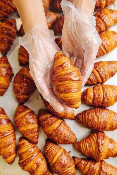 Baker, üzerinde bulundukları yüzeyden taze pişmiş altın kruvasan alıyor. Avuçlarında bir tane tutuyor. Üst manzara, yukarıdan çekim