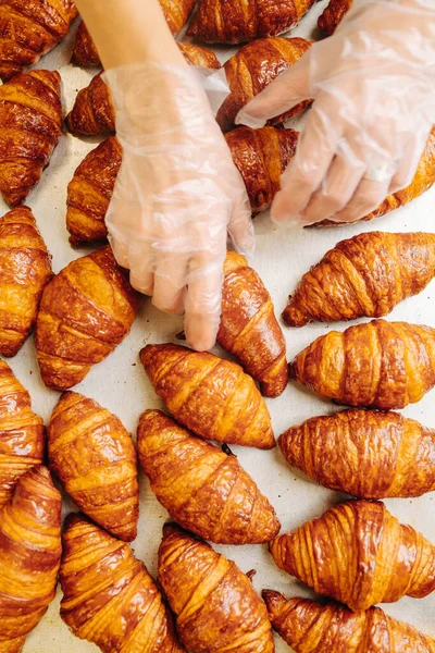 Baker üzerinde bulundukları yüzeyden taze pişmiş altın kruvasanları alıyor. Üst manzara, yukarıdan çekim