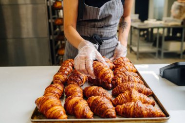 Baker serinlemek için metal tepsiye taze pişmiş altın kruvasan koyuyor. Ön görünüm