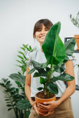 Elinde saksı bitkisiyle poz veren gururlu genç bir kadın.