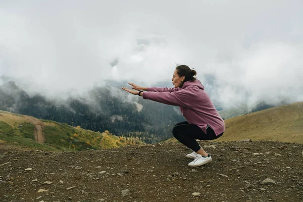 Молодая Женщина Делает Приседания Упражнения Высоко Горах Покрытые Короткой Травой — стоковое фото