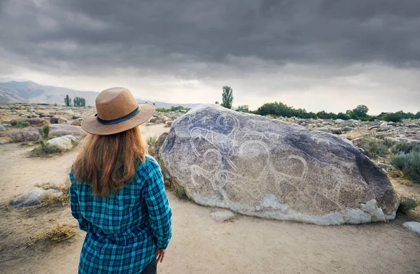 妇女戴着蓝色衬衫在露天博物馆附近的石头与古老的岩画山羊在吉尔吉斯斯坦 文化遗产博物馆 — 图库照片