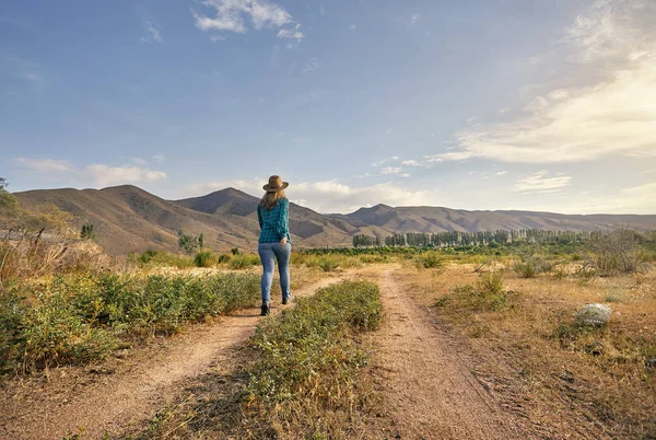 帽子と朝の農場の近くの田舎道を歩いてチェックの緑のシャツの女性 — ストック写真