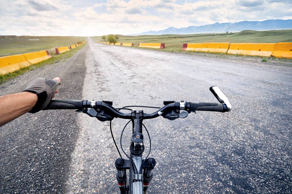 Rider in gloves holding handlebars of mountain bike on the highway road in the desert. 