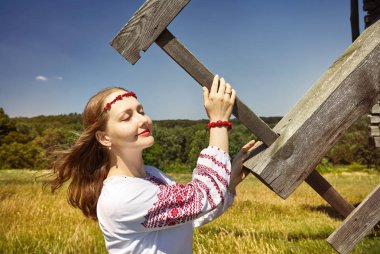 Mimarlık Müzesi Pirogovo'nde beyaz etnik gömlek ahşap rüzgar değirmeni bıçak tutan güzel Ukraynalı kız portresi. Kiev, Ukrayna