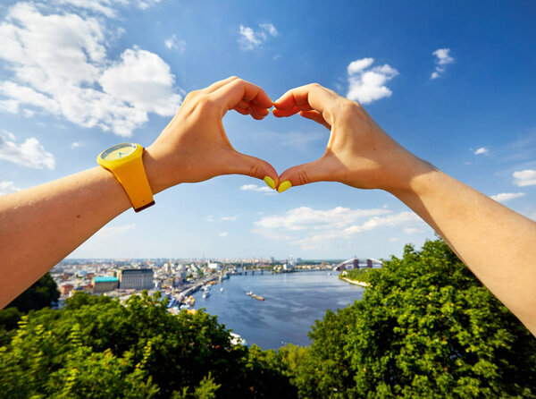 Woman hands in shape of heart with yellow watch against panorama of Kiev city downtown in Ukraine