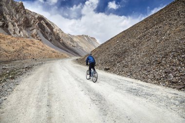 Mavi gökyüzü arka plan karşı yüksek dağlarda yolda adam dağ bisiklet sürmek.