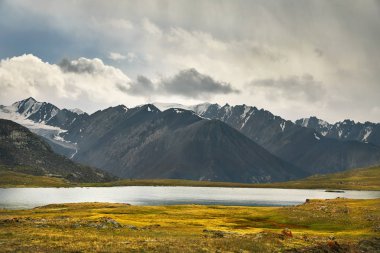 Beautiful Lake and Mountain Range in the valley against cloudy sky in Kyrgyzstan clipart