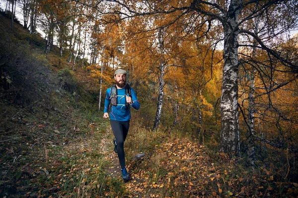 Runner athlete with beard running on the trail in the autumn yellow birch wood