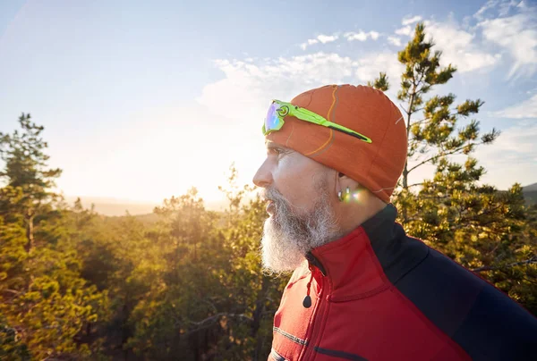 Portrait of old man with white beard in red shirt and in the forest at sunset