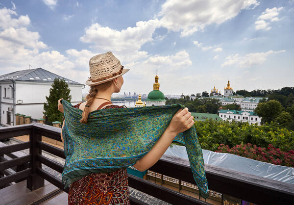 Woman in hat with scarf looking to the church with golden domes at Kiev Pechersk Lavra Christian complex. Old historical architecture in Kiev, Ukraine